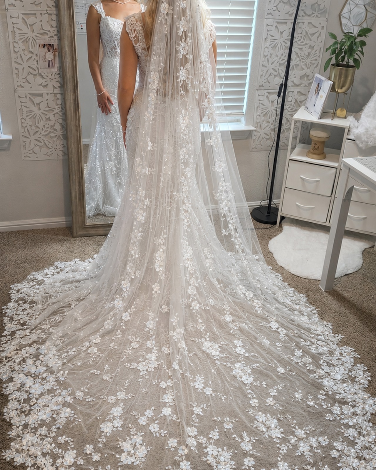 Novia con velo largo bordado frente a un espejo en el atelier